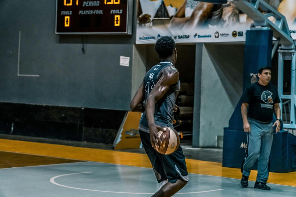 A basketball player in a green jersey holds a ball while looking toward the hoop on an indoor court during a game.