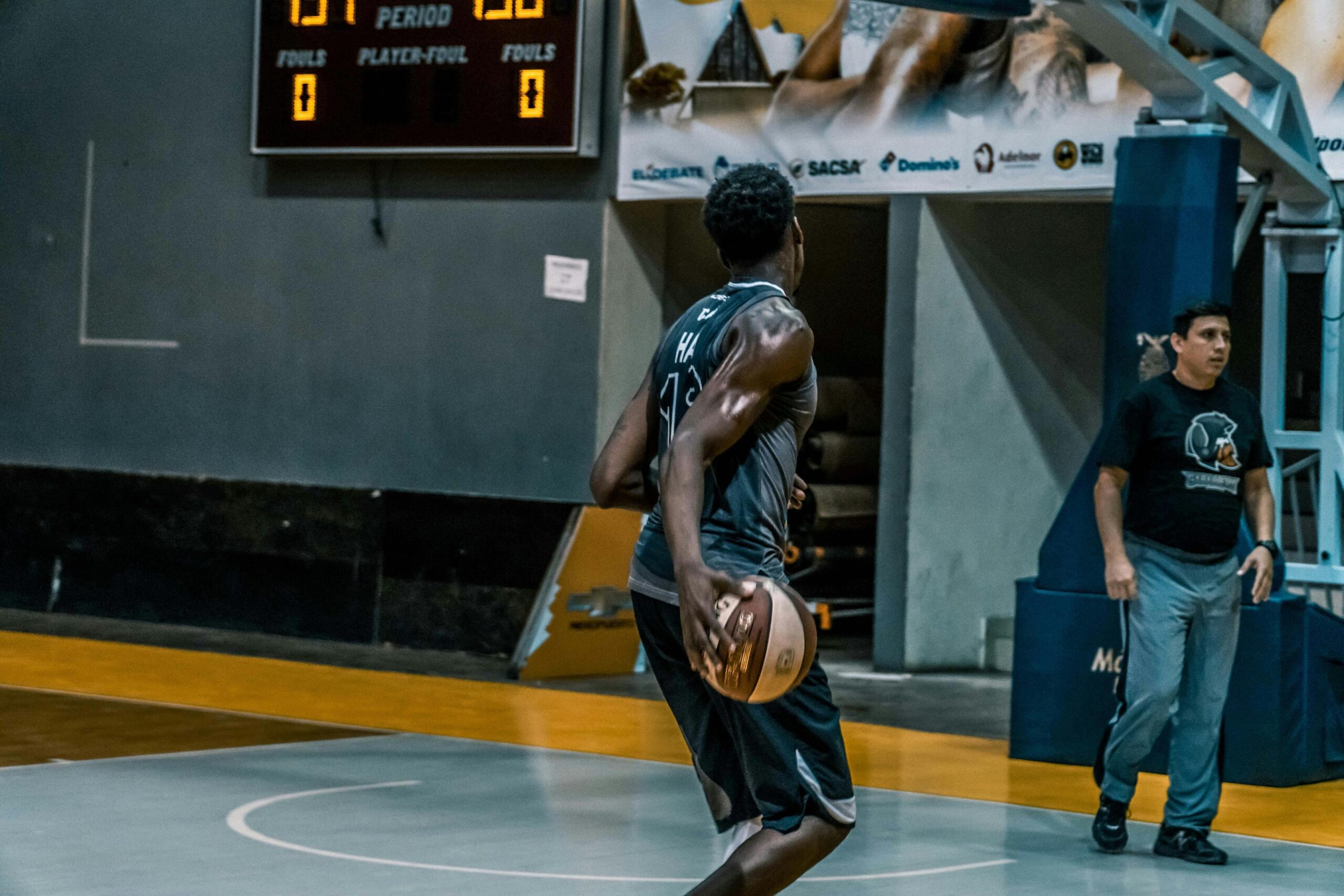 A basketball player in a green jersey holds a ball while looking toward the hoop on an indoor court during a game.