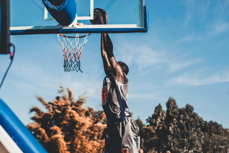 A basketball player in a grey jersey is captured mid-air during a powerful slam dunk.