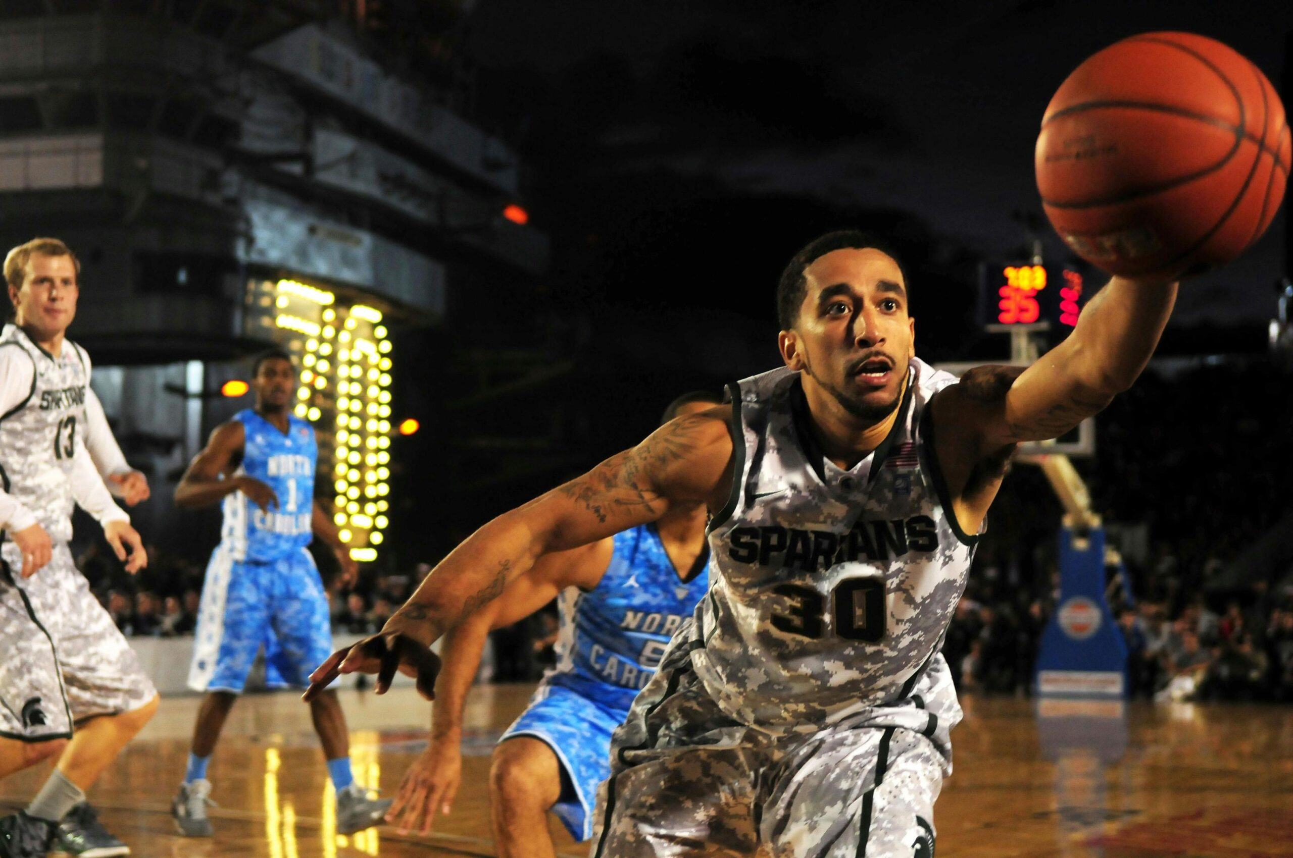 A basketball player in a camouflage jersey stretches to reach for the ball.