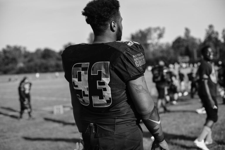 A black-and-white, rear-view shot of a football player wearing a jersey with the number 93, standing on a practice field.