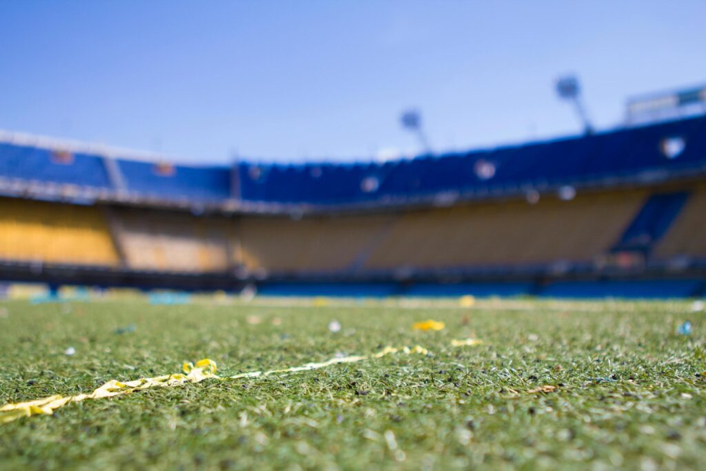 Yellow streamers rest on the green grass of a blurred, empty sports stadium with blue and yellow seating.