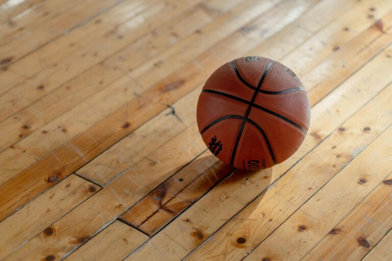 A close-up, high-angle shot of a classic basketball resting on a polished wooden gymnasium floor.