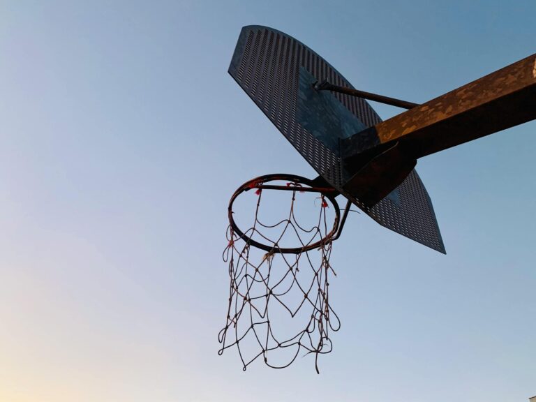 A low-angle shot of a weathered outdoor basketball hoop with a tattered net against a clear sky.