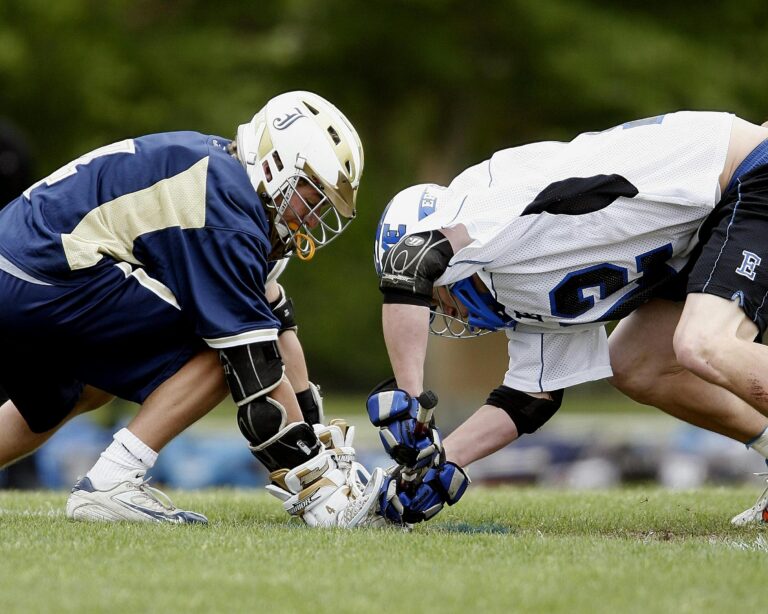Two players in helmets and protective gear crouch face-to-face on a field.