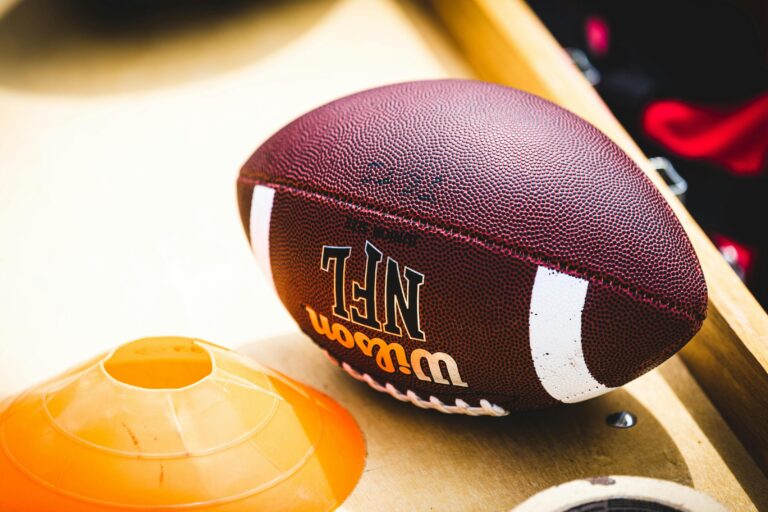 A close-up shot of a brown Wilson NFL football resting on a wooden surface next to an orange training cone.