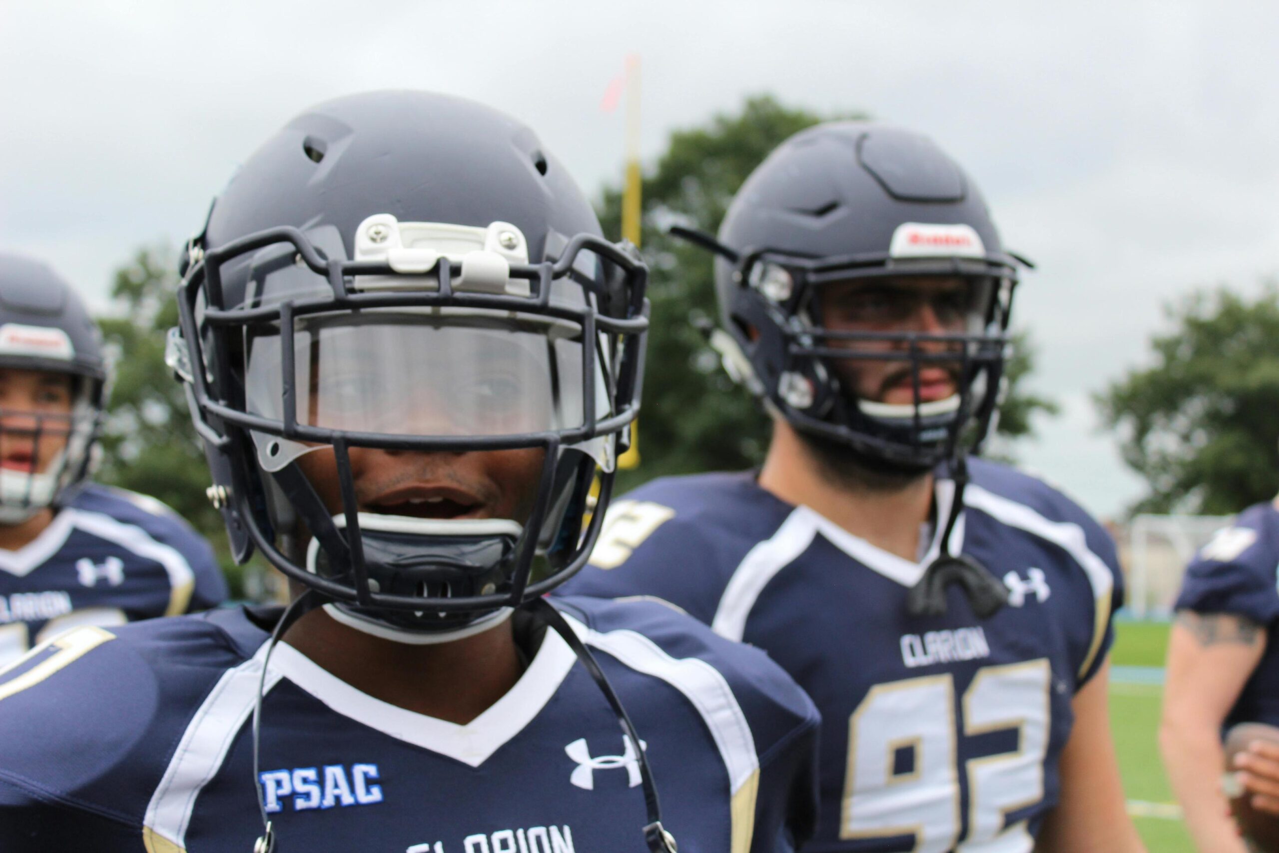 Close-up of American football players in navy and white "Clarion" uniforms wearing helmets with visors.