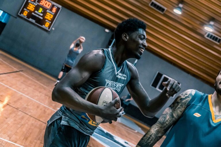 A basketball player smiles while holding a ball on an indoor court during a practice session or game break.