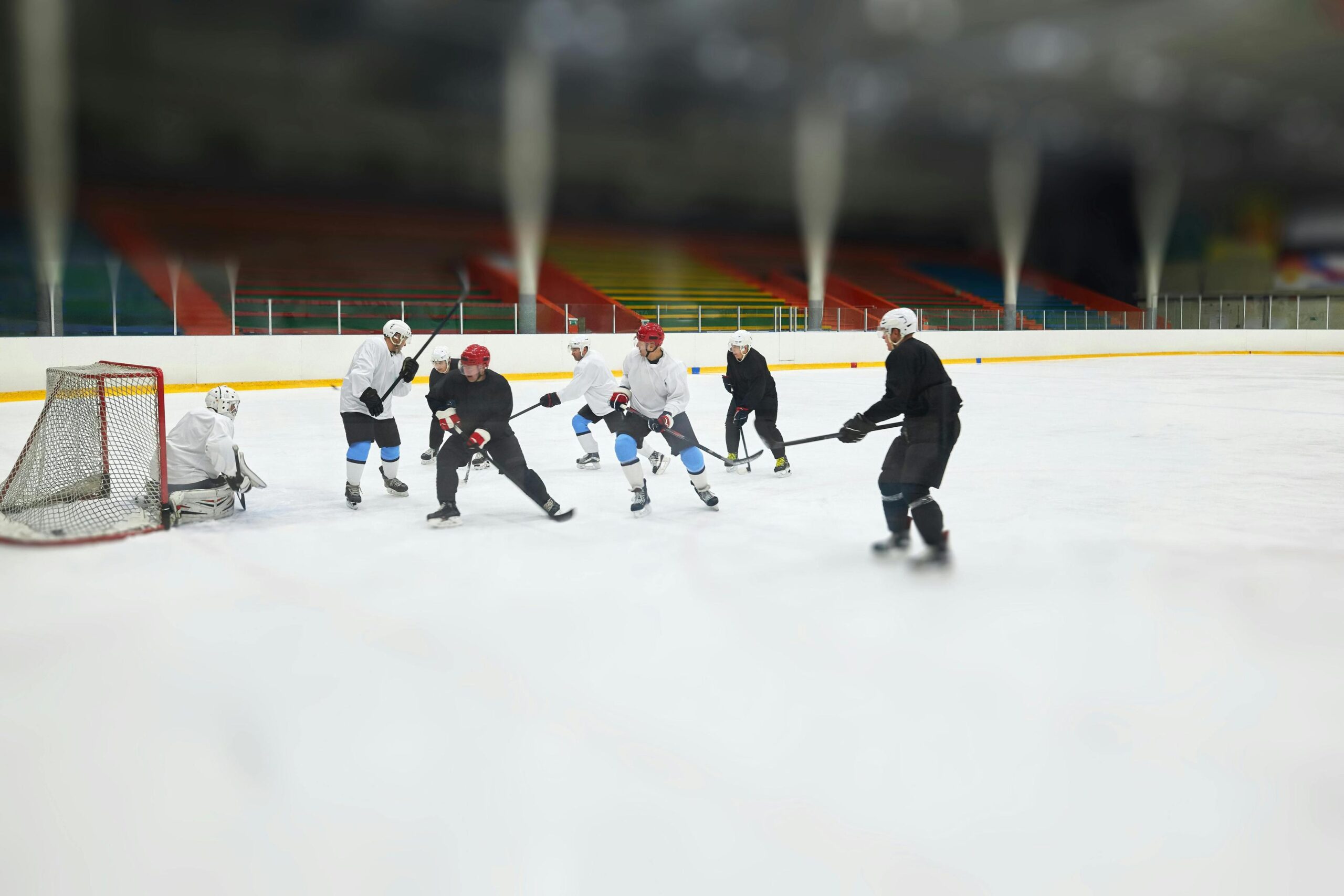 Ice hockey players in black and white jerseys compete for the puck during a game in a large, indoor arena.