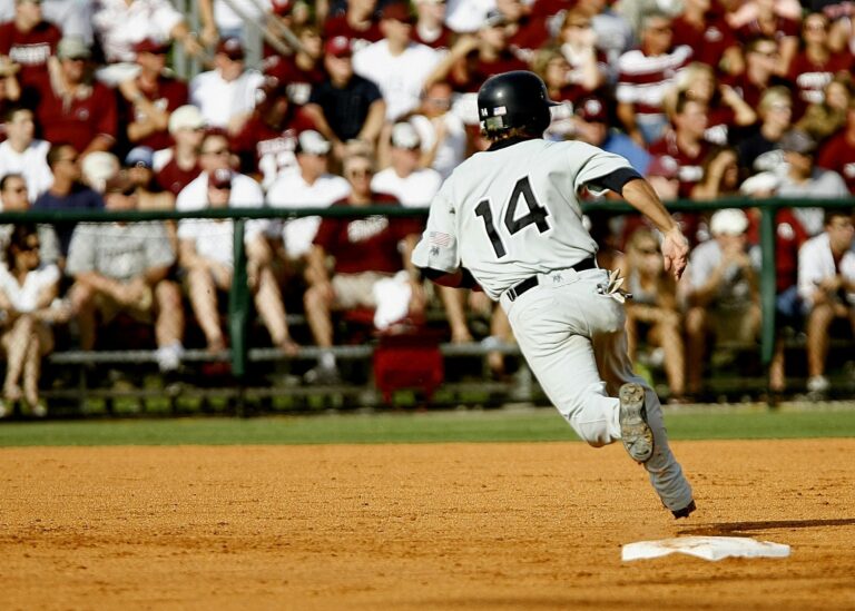 A baseball player wearing jersey number 14 sprints toward first base during a game in front of a seated crowd.