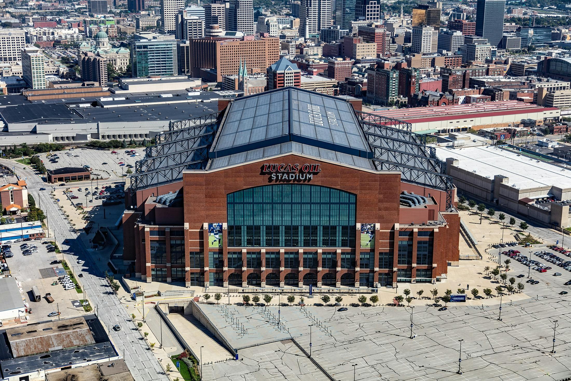 An aerial view of Lucas Oil Stadium, a large brick and glass domed sports venue situated within a city skyline.